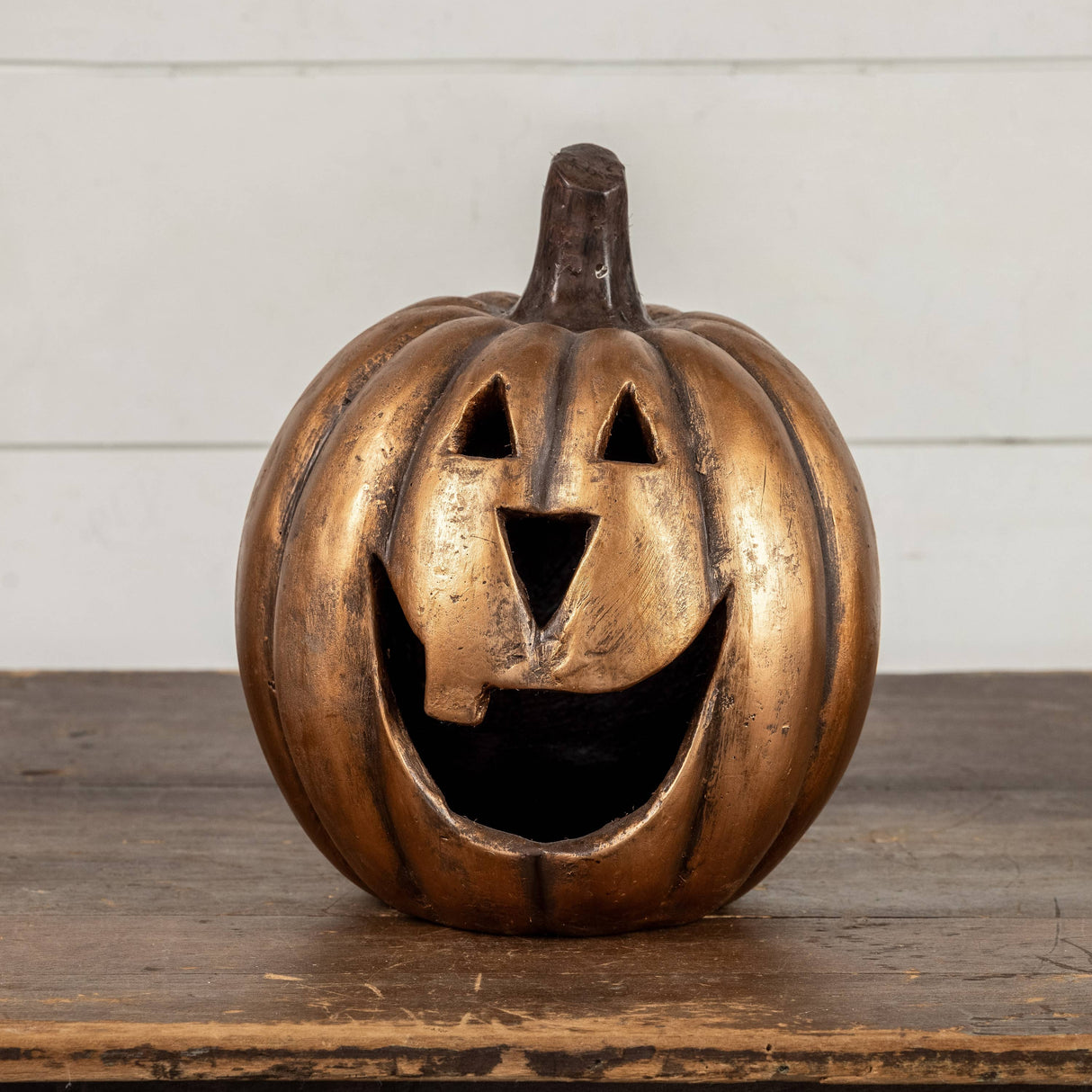 Gold metallic jack‑o’‑lantern pumpkin with a wide smiling face, styled on a wooden surface for Halloween décor.