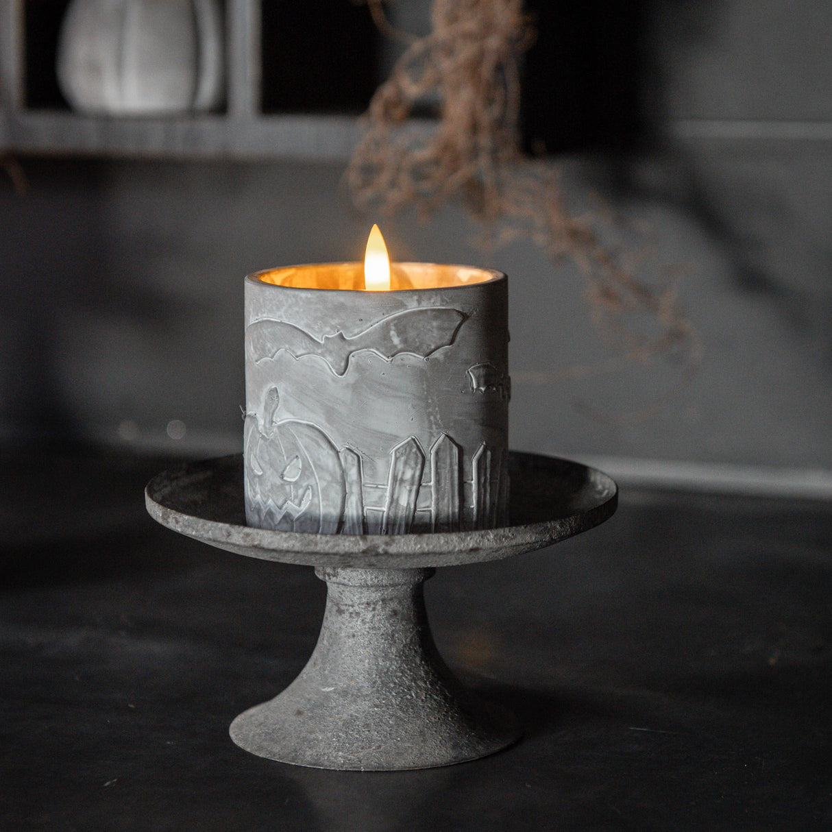 Decorative candle with bat design on a stand against a dark background