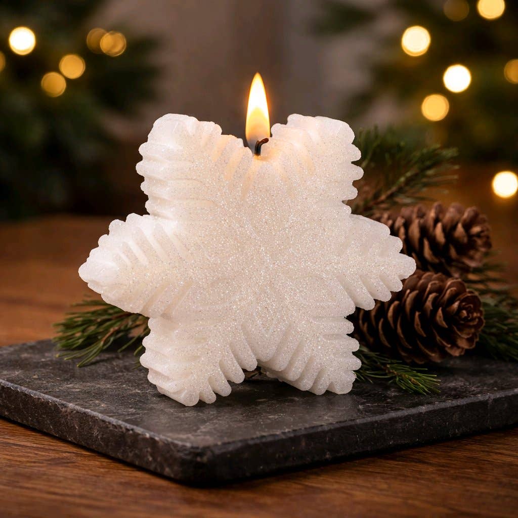White snowflake‑shaped candle glowing on a dark stone surface with pine branches and pinecones in a cozy holiday setting.