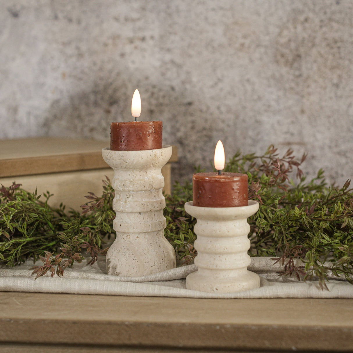 Set of two warm spiced‑fall moving‑flame tealight candles styled on ribbed cream holders with soft greenery.
