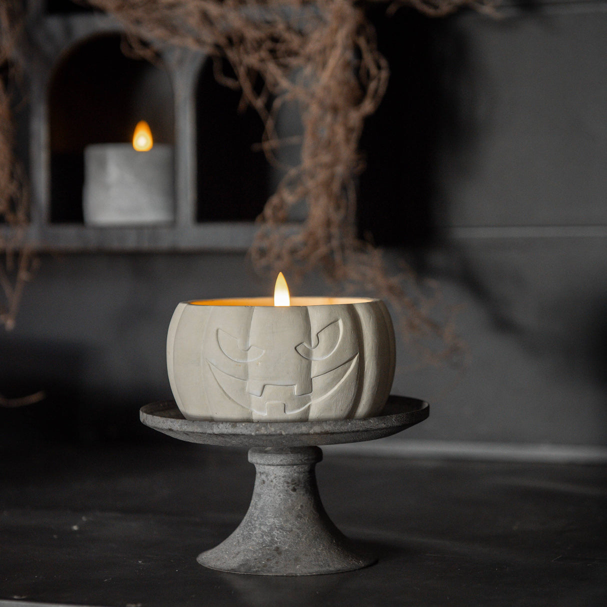 Cement pumpkin-shaped candle with a face on a stand in a dark setting