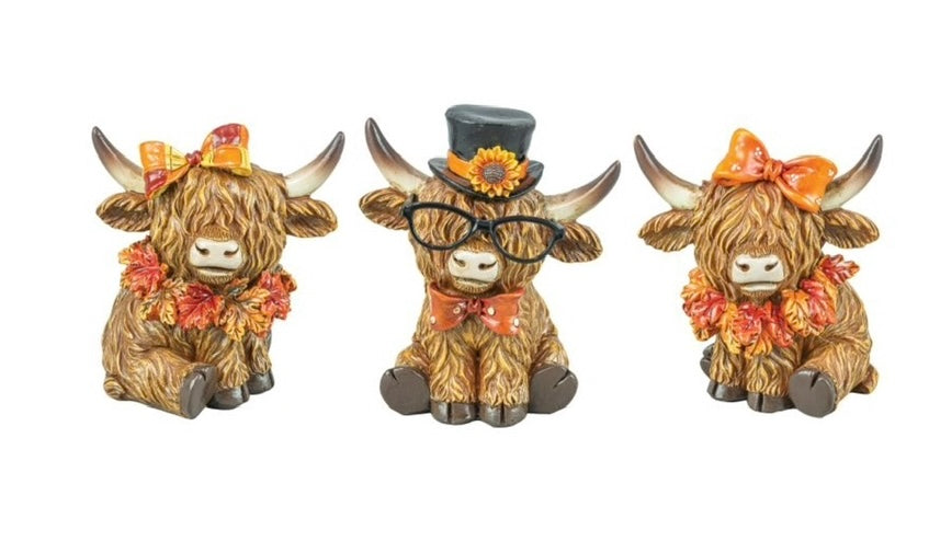 Three decorative cow figurines with Fall accessories on a white background