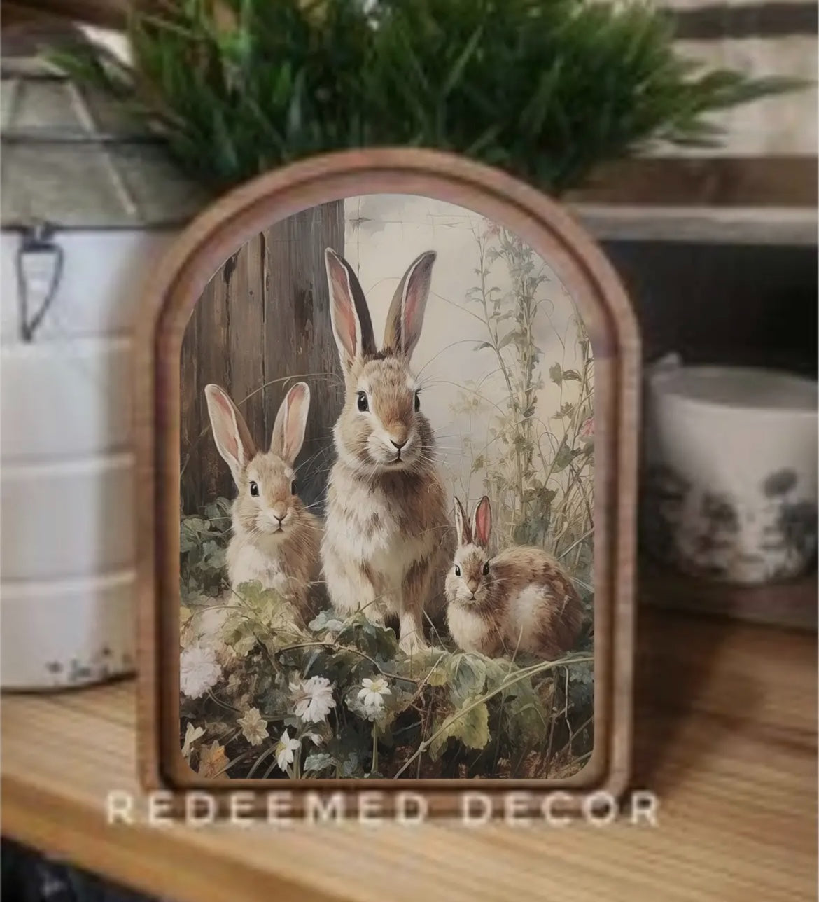 Three rabbits in a spring meadow with wildflowers, featured in an arched-top print from Redeemed Decor.