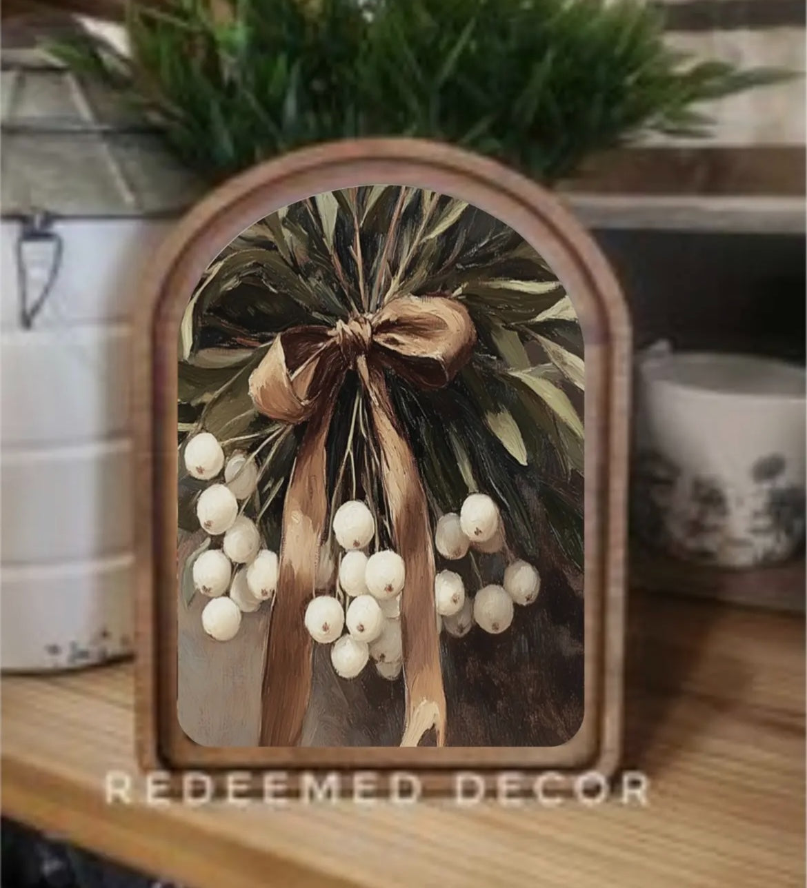 Decorative frame with a floral design featuring white berries and a brown bow, placed on a surface with a blurred background.