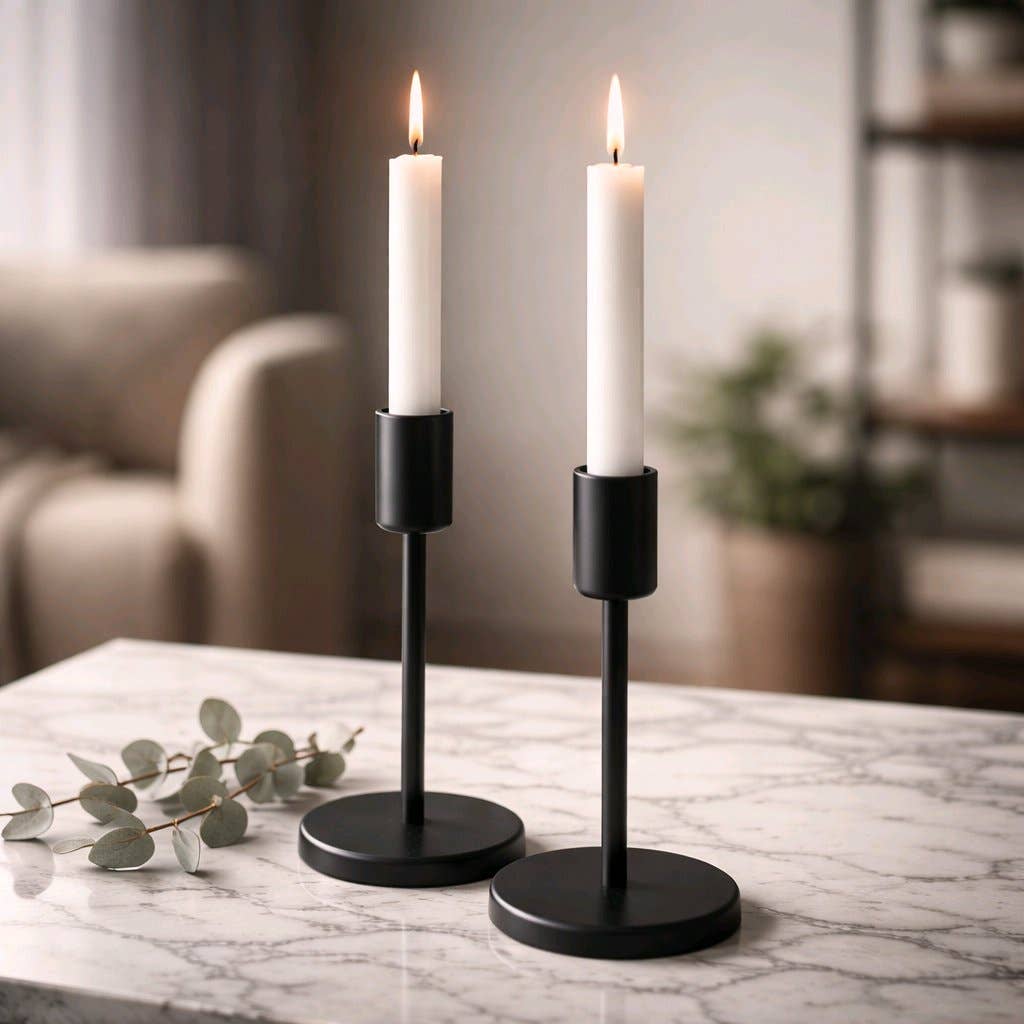 Two white taper candles in sleek black modern holders on a marble surface with soft, cozy background lighting.