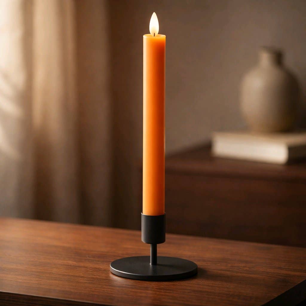 Pumpkin‑orange realistic‑flame taper candle glowing in a black holder on a wooden surface in a warm autumn setting.
