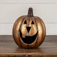 Gold metallic jack‑o’‑lantern pumpkin with a wide smiling face, styled on a wooden surface for Halloween décor.