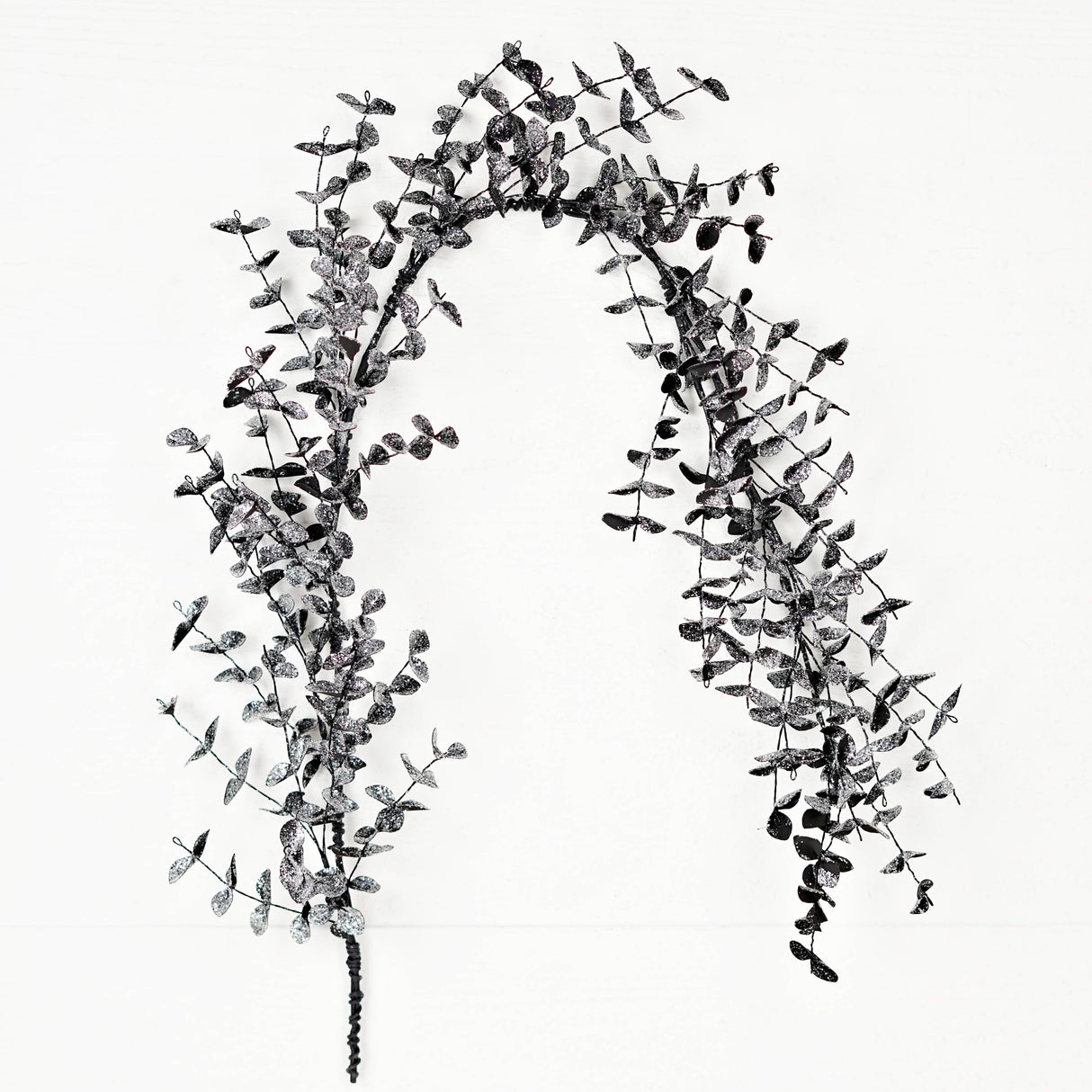 A slim black eucalyptus garland with delicate leaves and subtle glitter displayed against a white background.