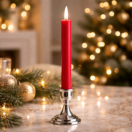 Red realistic‑flame taper candle glowing in a silver holder on a marble surface with blurred Christmas lights and greenery in the background.
