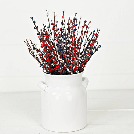 Red, white, and navy pip berry picks arranged in a white ceramic pitcher, creating a simple patriotic accent against a clean background.