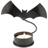 Metal bat candle holder with a flying bat silhouette illuminated by a tealight on a dark surface.