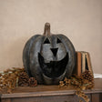 Decorative pumpkin with carved face on a wooden surface with books and pinecones.