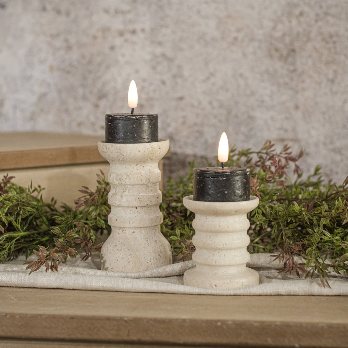 Set of two black 3D‑flame tealight candles styled on ribbed cream holders with soft greenery.