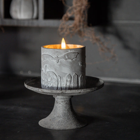 Decorative candle with bat design on a stand against a dark background