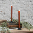 Pair of warm spiced‑autumnal moving‑flame taper candles styled in black holders with vintage books and greenery.