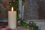 Cream LED pillar candle glowing beside a window, surrounded by a trailing green vine and rustic décor for a warm, cozy ambiance.