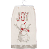 A cream-colored fabric tea towel hanging on a white plastic hanger. The towel features a hand-drawn style snowman wearing a red and white striped hat and scarf, with the word 'JOY' written above in a red-and-white striped font.