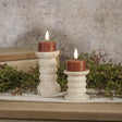 Set of two warm spiced‑fall moving‑flame tealight candles styled on ribbed cream holders with soft greenery.