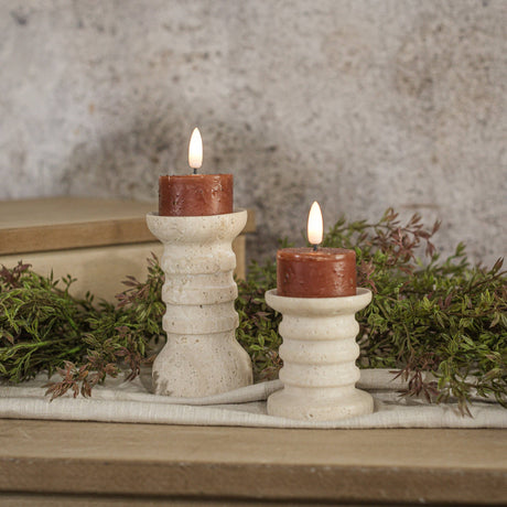 Set of two warm spiced‑fall moving‑flame tealight candles styled on ribbed cream holders with soft greenery.