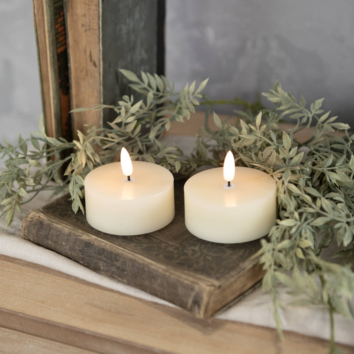 Two lit candles on an old book with greenery in the background