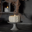 Cement pumpkin-shaped candle with a face on a stand in a dark setting