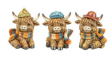 Three decorative Highland cow figurines wearing hats and scarves on a white background