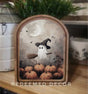 Arched framed canvas featuring a ghost wearing a witch’s hat flying on a broom over pumpkins with a crescent moon and bats.