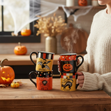 Halloween-themed mugs on a wooden table with pumpkins and a person holding one mug.