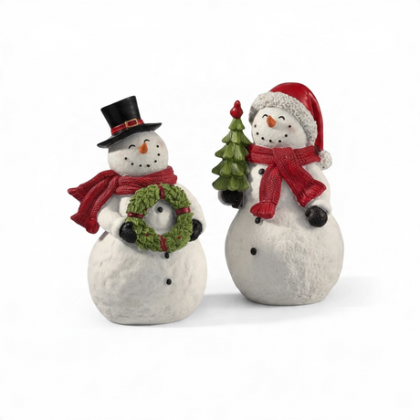 Two flocked snowman figurines feature a soft snow-covered texture and festive red scarves. One snowman wears a black top hat and holds a green holiday wreath, while the other wears a red Santa hat and holds a green Christmas tree. Both figurines are crafted from resin with a realistic flocked finish that resembles freshly fallen snow.
