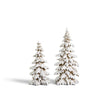 A set of two snowy woodland evergreen trees feature heavily snow-covered branches with realistic layered detailing. The natural tree trunks and branches peek through the snowy finish, creating the appearance of freshly snow-laden evergreens in a winter forest. The set includes two coordinating trees, with the tallest measuring 20 inches high.