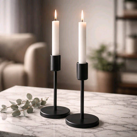 Two white taper candles in sleek black modern holders on a marble surface with soft, cozy background lighting.