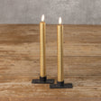 Two gold flameless candles with black bases on a wooden surface.