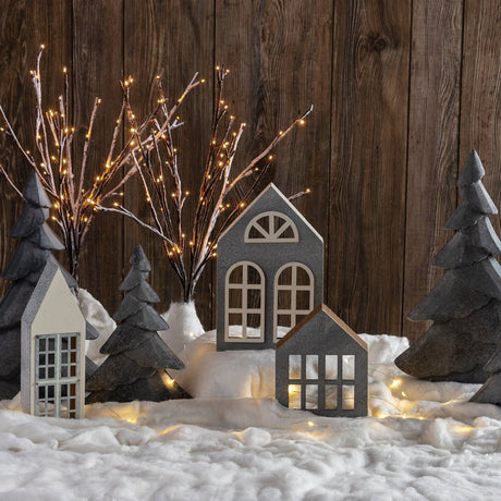 Cozy winter village display with miniature houses, evergreen trees, warm string lights, and a soft layer of artificial snow creating a festive holiday atmosphere.