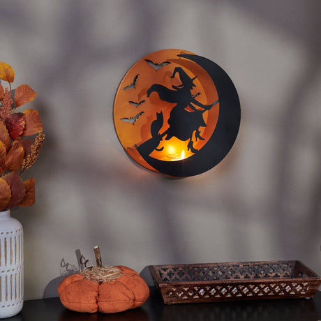 Metal wall candle holder featuring a witch flying across the moon with bat accents, illuminated by a tealight for warm Halloween ambiance.