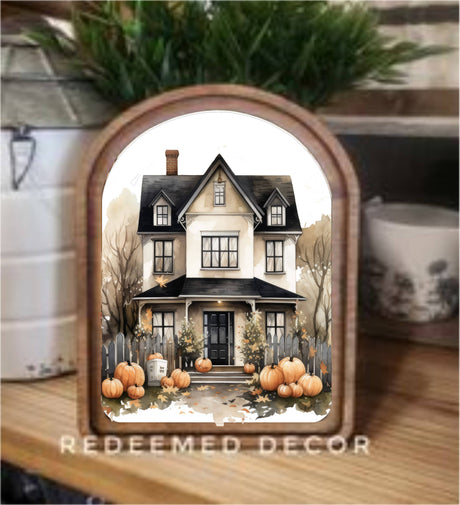 Arched framed canvas featuring a rustic two‑story house surrounded by pumpkins, bare trees, and autumn leaves.
