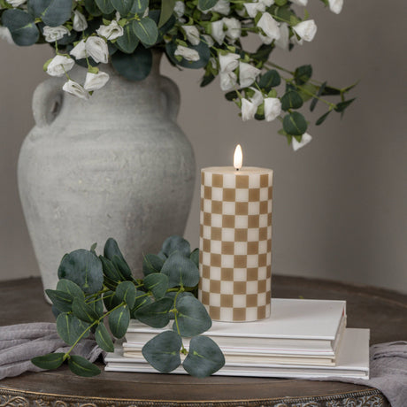 6" Pillar: Gold checked LED pillar candle with realistic 3D flame styled with books, greenery, and a ceramic vase.