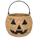 Round woven jack‑o‑lantern basket made of water hyacinth with black faux‑leather handle and cutout pumpkin face.