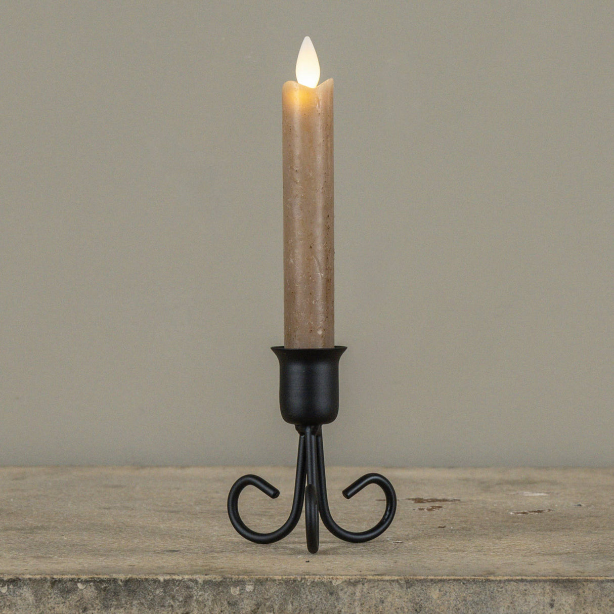 Black metal Serafina taper candle holder with decorative curved legs, shown styled with a taper candle (not included).