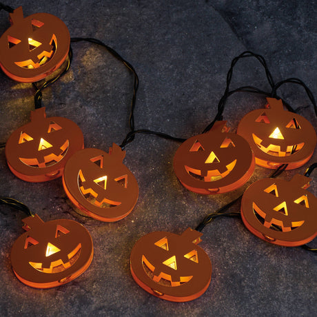 String of glowing metal jack‑o’‑lantern lights on a dark surface, each pumpkin illuminated with warm Halloween ambiance.